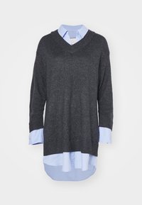 Maglione grigio scuro a collo a V con maniche lunghe, realizzato in tessuto a maglia texture. Camicia azzurra sotto con dettagli dei bottoni e polsini visibili.