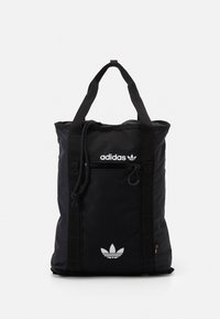 Svart Adidas totebag med dubbla handtag, framficka med dragkedja, vit logotryck och dragsko-detalj på vit bakgrund.