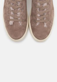 Un par de zapatillas de ante taupe con cordones beige y suelas de goma blanca, que presentan sutiles detalles de piel a lo largo de los bordes de la lengua.