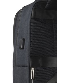 Gray fabric backpack with a mesh panel, zip closure, and silver hardware. Features adjustable straps and a textured surface detail.