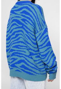 Blå och turkos stickad tröja med zebramönster, avslappnad passform och ribbad nederkant och ärmar. Slät textur med oversized ärmar.