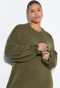 Übergroßer, olivgrüner Strickpullover mit ribbeligem Rundhalsausschnitt und voluminösen Ärmeln. Besticht durch strukturierten Stoff und geraffte Manschetten.