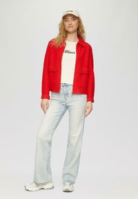 Rote, Wolle-Mischung Jacke mit zwei Brusttaschen, kombiniert mit einem weißen Grafik-T-Shirt, hellblauen hochgeschnittenen Jeans und grauen Sneakers.