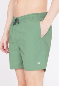 Gröna badshorts tillverkade av lätt material. Har en elastisk midja med dragsko, sidofickor och en liten logotyp på vänster ben.