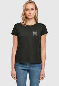 Tricou din bumbac negru cu mâneci scurte, guler rotund și un imprimeu alb pe piept. Materialul pare moale și casual.