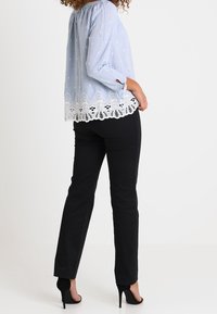 Lyseblå off-shoulder bluse med hvidt broderet blonder og hvide polkaprikker, kombineret med sort tætsiddende bukser og sorte hæle.