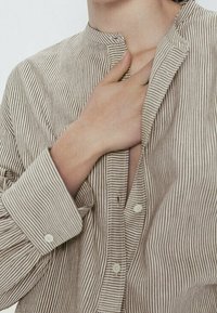 Chemise à rayures beige et crème, à boutons, avec col mao, manches longues et coupe d écontractée, boutons et coutures apparents.