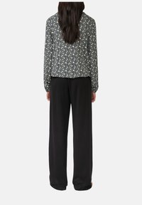 Langärmlige Bluse mit einem mehrfarbigen geometrischen Muster, kombiniert mit locker sitzenden schwarzen Hosen. Strukturiertes Material, entspannte Silhouette.
