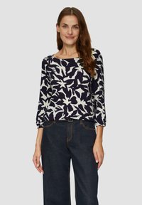 Navy-blaues Langarmoberteil mit einem weißen abstrakten Blumenmuster, rundem Ausschnitt und lockerer Passform, kombiniert mit dunkelblauen weiten Jeans.