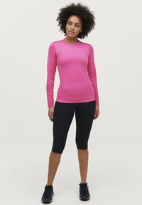 Lyserød langærmet træningstop med tætsiddende design, parret med sorte knælange leggings. Har reflekterende detaljer på ærmerne og en glat overflade.