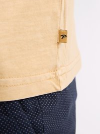 Tricou galben deschis cu o etichetă pe lateral, asortat cu pantaloni bleumarin cu un model punctat. Material din bumbac, croi casual.