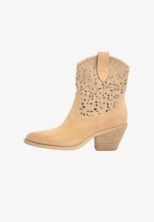 Beige ruskind ankel cowboystøvle med stablet træsål og overdelen dekoreret med små metalliske nitter og perforerede blomster mønstre.