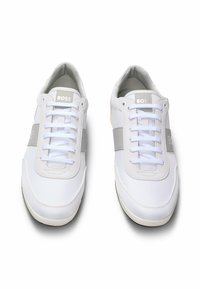 Sneakers bianchi con tomaia in rete, lacci bianchi piatti, dettagli grigi e una patch con logo sulla linguetta. Punta arrotondata e suola ammortizzata.