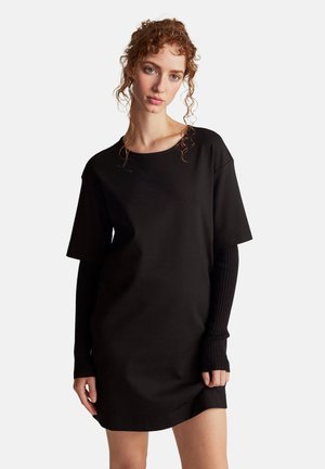 Vestido negro de manga corta, con acentos de mangas largas acanaladas. Corte sencillo y relajado con escote redondo y una textura suave.