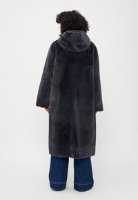 Manteau en fausse fourrure de couleur gris foncé, avec une capuche et des manches longues. Le design est surdimensionné, offrant un ajustement confortable et de la chaleur.