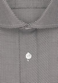 Camicia bianca e nera con motivo a zigzag, colletto standard e un unico bottone bianco sul davanti.