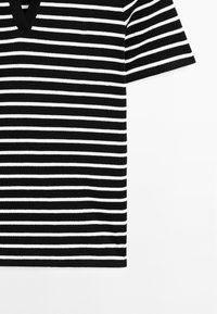 Haut en maille rayé horizontal noir et blanc à manches courtes avec col en V sur fond blanc.