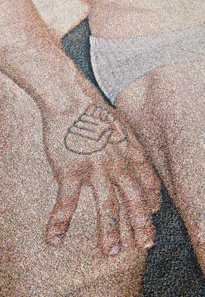 Close-up of a hand with a heart tattoo on the palm, resting on a person's thigh. Skin tones light with a smooth texture, minimal clothing visible.