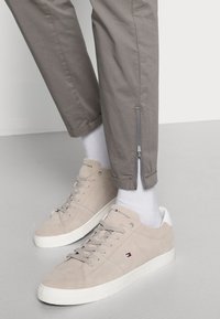 Sneakers in suede grigio chiaro con suole e lacci bianchi. Abbinati a pantaloni grigi con dettagli a zip sui polsini e calze bianche.