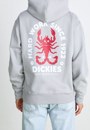 Person trägt einen grauen Hoodie mit rotem Hummer-Design und weißem Text "Hard Work Since 1922 Dickies Fort Worth, Texas" auf dem Rücken.