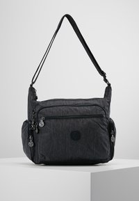 Gray fabric shoulder bag with multiple zippered compartments, adjustable strap, and circular logo on the front for added detail.