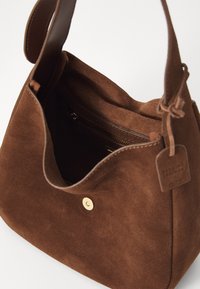 Brown suede handbag with a soft texture and open top. Features a magnetic closure and a leather tag. Interior includes a zipped pocket.