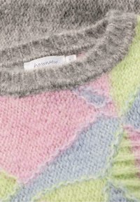 Multikleurige gebreide trui met pastelroze, -blauwe en -groene vlekken en een zachte grijze kraag. Etiket zichtbaar nabij de halslijn.