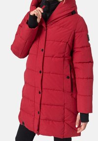 Red padded jacket with a high collar, black zipper, and side pockets. Features button closure and contrasting black cuffs. Durable fabric.