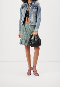 Chaqueta de mezclilla, top negro corto, falda rizada verde con lunares, bolso negro y tacones altos morados con tiras.