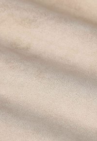 Gros plan sur un tissu en suédine beige avec une texture douce et veloutée, présentant de subtiles variations de lumière et d'ombre à la surface.