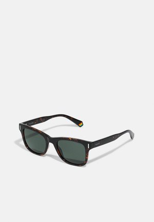 Óculos de sol em padrão tartaruga castanha com lentes verde escuras, forma quadrada e hastes pretas planas com um pequeno detalhe em arco-íris do lado esquerdo.