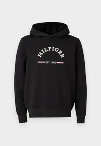 Felpa nera in cotone, con un logo frontale bianco che riporta "HILFIGER" e "EST. 1985", accompagnato da strisce rosse e bianche.