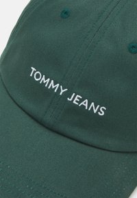 Căciulă de baseball din bumbac verde, cu text brodat alb "TOMMY JEANS", brie curbată și detalii cusute.