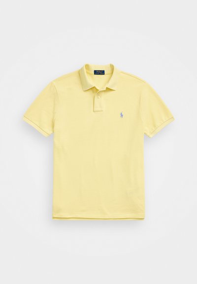 Polo majica iz mehkega rumenega bombaža s ovratnikom, kratkimi rokavi in majhnim modrim logotipom na levem prsnem predelu. Klasična prileganje.
