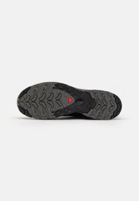 Black hiking shoe sole with a rugged grey tread pattern. Features a red triangular accent and a textured design for grip.