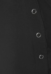 Roupa de algodão preta com ilhoses de metal ao longo da costura lateral. A textura parece suave, com uma silhueta ajustada.