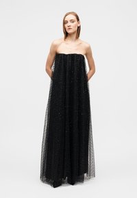 Black strapless gown made of tulle with a loose, flowing silhouette, featuring textured accents and an open back design.