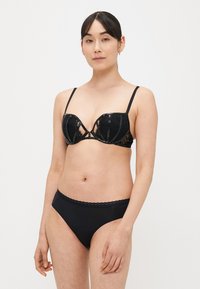 Set di lingerie in pizzo nero con reggiseno balconette con dettagli lucidi e spalline sottili, abbinato a slip a vita alta coordinati.