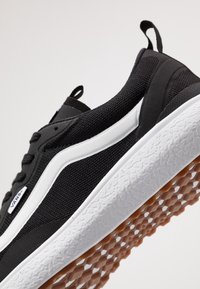 Baskets Vans noires avec bande latérale blanche, semelle blanche texturée et semelle extérieure marron à motif gaufré, vues de côté et de dessous.