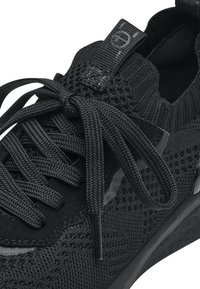 Botte de sport noire avec une tige en tricot, des lacets ronds et des accents réfléchissants. Surface texturée, semelle rembourrée et boucle de traction au talon.