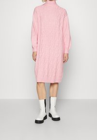 Pink knitted sweater dress with cable pattern, high neckline, and ribbed cuffs, paired with white and black ankle boots.