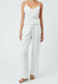 Top bianco senza maniche con scollo a V, abbinato a pantaloni bianchi larghi con cordoncino. Texture liscia, design minimale e spalline piatte.