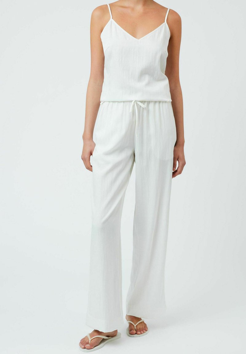 Top bianco senza maniche con scollo a V, abbinato a pantaloni bianchi larghi con cordoncino. Texture liscia, design minimale e spalline piatte.