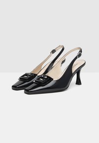 Tacchi slingback in vernice nera con punta affusolata, caratterizzati da una fibbia quadrata decorativa e un tacco medio. Texture liscia.