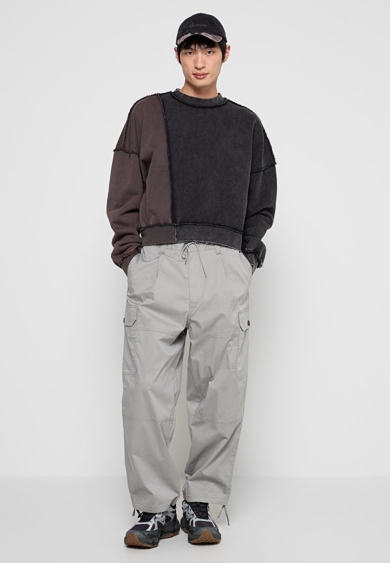 Suéter grande en negro y gris con costuras deshilachadas, combinado con pantalones cargo en gris claro. Calzado con diseño en negro y blanco con detalles en marrón.