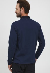 Námornícky polo tričko s dlhým rukávom a klasickým golierom, s diskrétnym pruhovaným detailom na golieri a rovnou spodnou časťou.