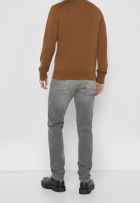 Brun strikket sweater med rund halsudskæring, kombineret med grå jeans. Jeansene har et let slidt udseende og bæres med sorte ankelstøvler.