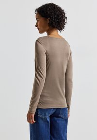 Haut à manches longues et ajusté en tissu taupe doux avec un col rond, associé à un jean en denim bleu ample. Design simple et sans couture.