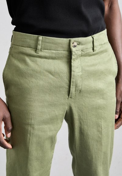 Lichtgroene linnen broek met een platte voorkant, riemlussen en een enkele knoopsluiting. De stof heeft een textuurafwerking.