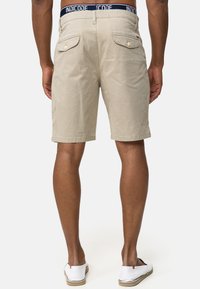 Pantalones cortos beige hasta la rodilla hechos de tela texturizada, con una cinturilla que presenta una marca en azul, y dos bolsillos traseros con botones.
